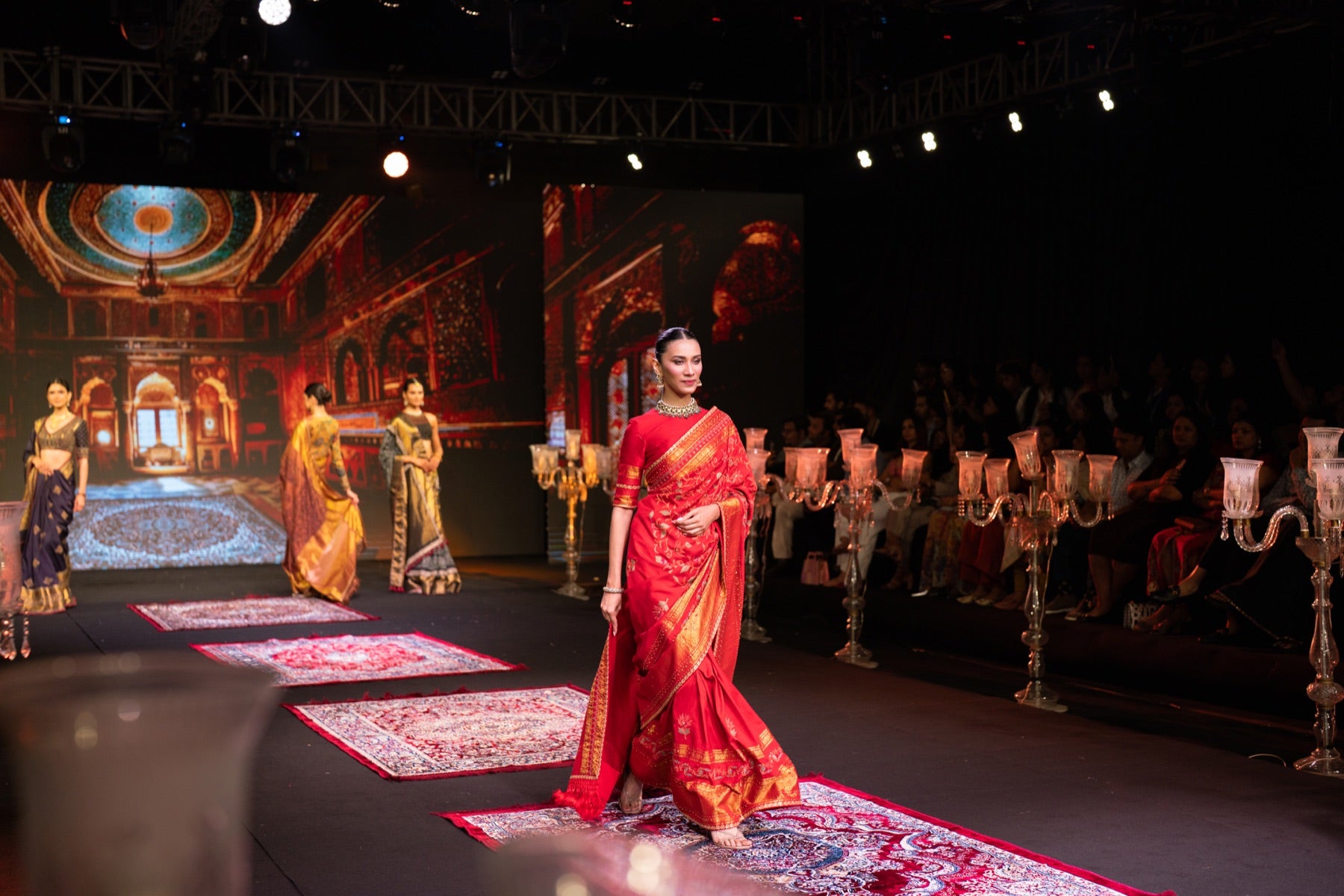 Model in a red saree against a blue palace projection backdrop