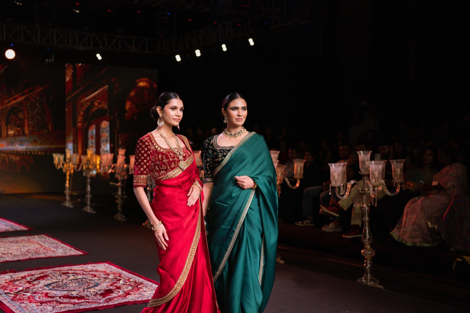Two models in red and teal sarees walking together