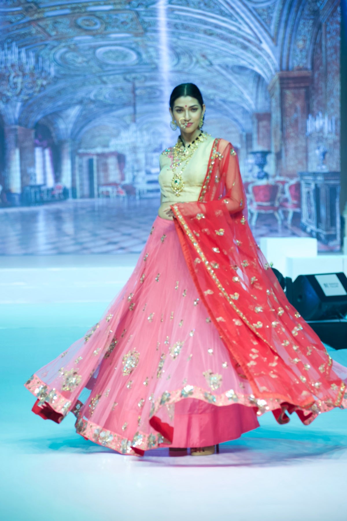 Model in a coral lehenga with a gold blouse, mid-twirl