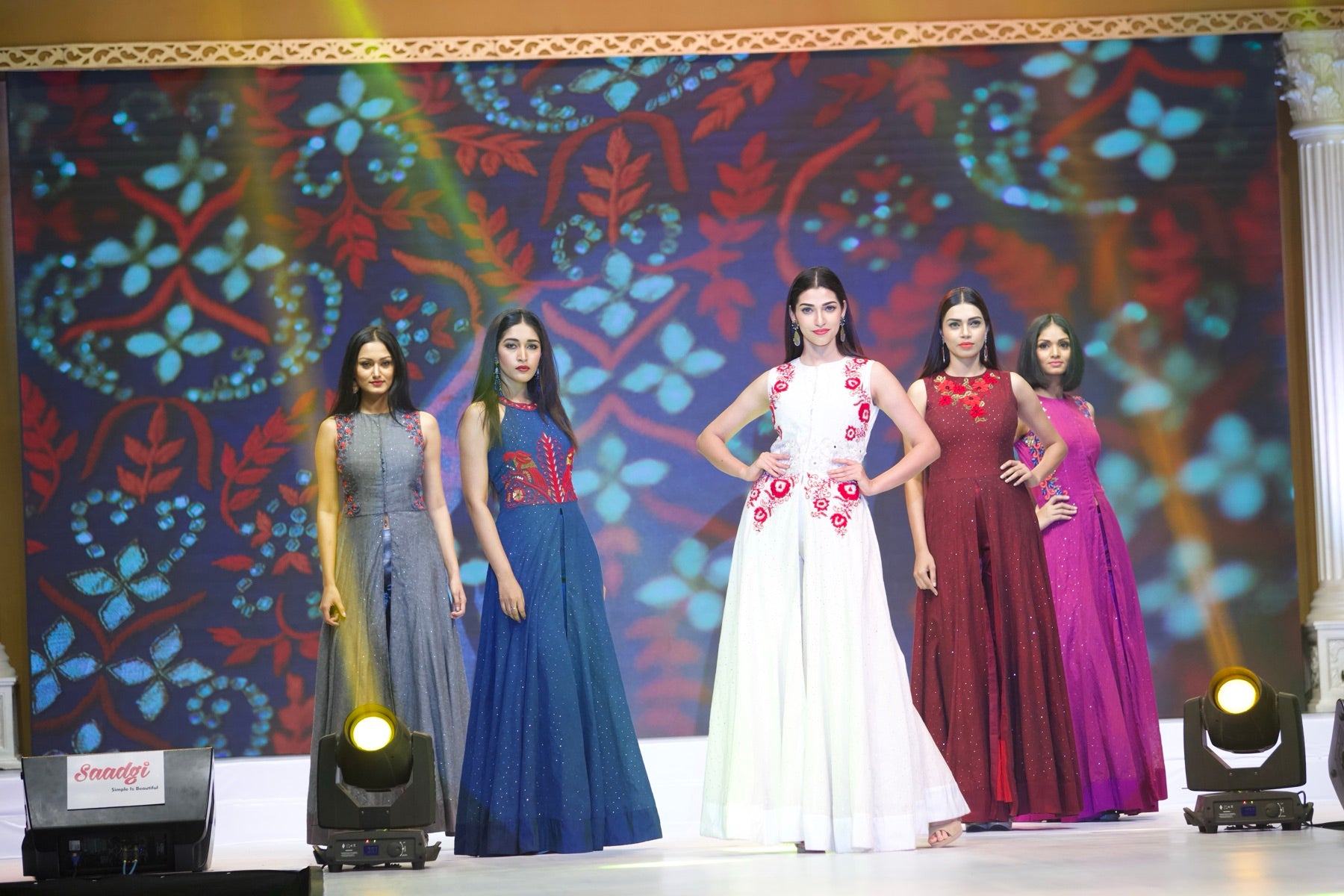 Five models in a mix of gowns and dresses on the runway